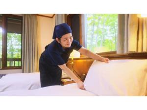 青森Sukayu Onsen Hakkoda Hotel - Vacation STAY 66846v的一位女性在旅馆房间做床