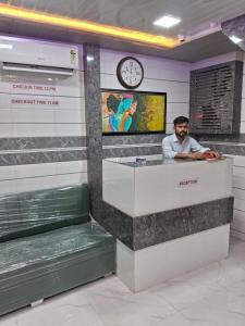 孟买Hotel Sai Plaza, Chembur Mumbai的坐在柜台上,坐在一个有钟表的房间的人