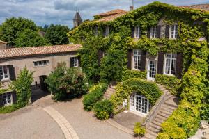 弗卢尔Château de Floure - Hôtel, restaurant, SPA et piscine extérieure chauffée的一座常春藤覆盖的建筑,设有白色的窗户和灌木丛