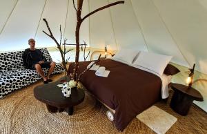 MeraFinca de la Vaca - Glamping & Camping的坐在一张大床旁边的沙发上的人
