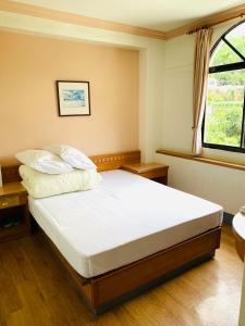 古坑永利饭店的一间卧室配有一张带白色床单的床和一扇窗户。