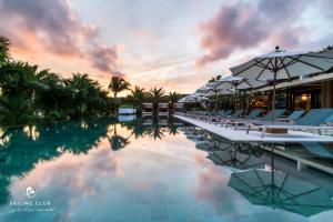 富国Sailing Club Signature Resort Phu Quoc的日落时分带椅子和遮阳伞的游泳池