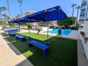 贝纳尔马德纳Luxury beachfront apartment in Benalmadena Costa的庭院设有蓝色长椅和遮阳伞