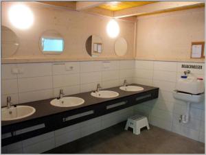 德兰斯克Baumzeltdorf OSTSEEBREEZE direkt am Strand的一间带三个盥洗盆、卫生间和镜子的浴室