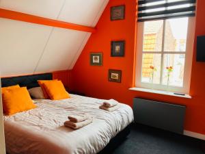 济里克泽B&B with or without De Schuur的一间卧室设有橙色的墙壁和一张带毛巾的床