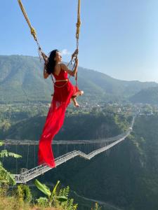 KusmaThe Cliff Resort Pokhara Kushma的穿着红色衣服的女子在绳桥上摇晃