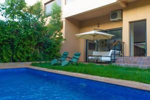 马拉喀什New villa in Marrakech palmeraie的房屋旁的游泳池配有椅子和遮阳伞