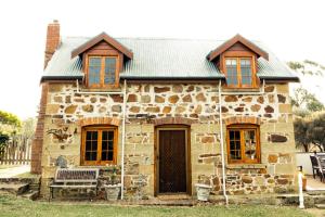 Little SwanportThe Blacksmith's Cottage at Lisdillon Vineyard的石头房子前面有长凳