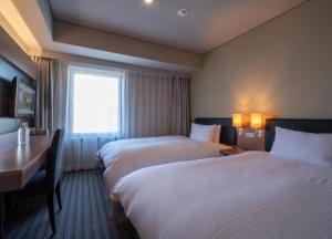 大阪Prince Smart Inn Osaka Yodoyabashi的酒店客房设有两张床、一张书桌和一个窗户。