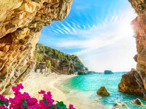 科孚镇Pentofanoro Central Studio - Corfu Cozy Getaway的从带粉红色花卉的洞穴欣赏海滩美景