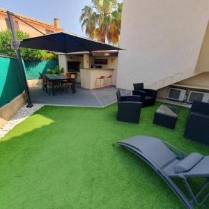 马里尼亚讷Joli haut de villa 3 chambres climatisé avec jacuzzi的后院设有绿色草坪、椅子和雨伞