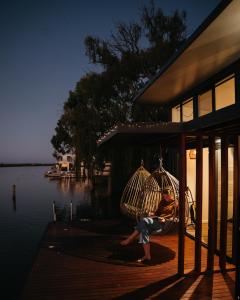 White SandsArk-imedes - Unique float home on the Murray River的坐在水边门廊上摆动的人