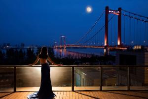 武汉武汉世茂希尔顿酒店 - 长江江景的站在阳台上望着一座桥的女人