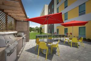 莱克兰Home2 Suites By Hilton Lakeland的一个带桌椅和红色遮阳伞的庭院
