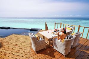 南马累环礁SAii Lagoon Maldives, Curio Collection By Hilton的坐在海边甲板上桌子上的女人