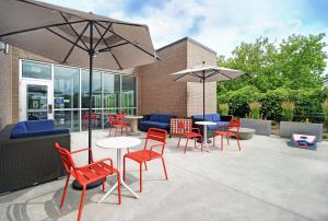 肯特伍德Tru By Hilton Grand Rapids Airport的一个带红色椅子、桌子和遮阳伞的庭院