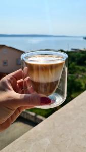 帕什曼Orkula Apartments的手持一杯咖啡在海洋前边