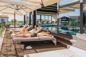 布耶San Servolo Wellness Resort - Adults Only的两个人躺在度假村的游泳池里躺椅上