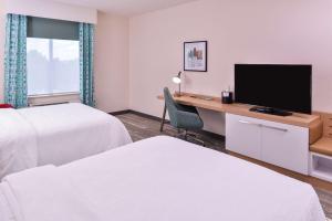 堪萨斯城Hilton Garden Inn Kansas City Airport Mo的酒店客房设有两张床和一张书桌及电视