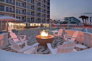 奥蒙德海滩Home2 Suites Ormond Beach Oceanfront, FL的酒店前方设有带椅子和火坑的庭院。