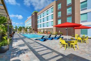 迈尔斯堡Home2 Suites by Hilton Fort Myers Colonial Blvd的一个带桌椅和红色遮阳伞的游泳池