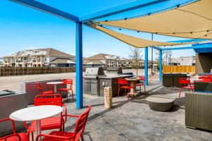 米德兰Tru By Hilton Midland, Tx的庭院设有红色的桌椅和蓝色的天篷