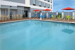 肯纳Home2 Suites By Hilton Kenner New Orleans Arpt的一座带椅子和遮阳伞的游泳池位于一座建筑旁边