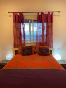 西迪拉哈尔Une vue imprenable sur l'océan !的一间卧室配有一张带红色窗帘的床和一扇窗户