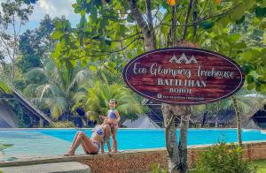 BalilihanEco Glamping Treehouses Closest Resort To All Tourist Attractions的两名妇女站在一个度假村的游泳池旁