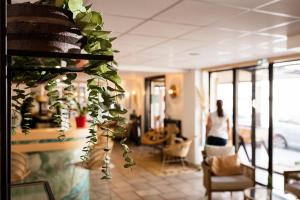 鲁西隆地区卡内Hôtel Les Sables - Urban Style - by Logis Hotels的带着植物穿过房间的妇女