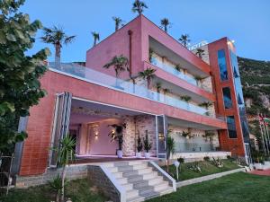 伏罗拉Festim Villa Hotel的一座粉红色的建筑,上面有棕榈树