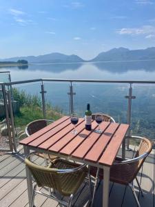 格伦科Loch Linnhe Waterfront Lodges with Hot Tubs的阳台上的木桌和两杯葡萄酒