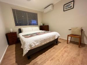 弗兰克斯顿Cosy 3 bedroom family home near beach and shops的一间卧室设有一张床、一个窗口和一把椅子