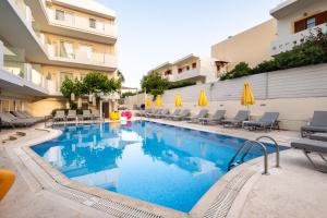 罗希姆诺Dimitrios Beach Hotel Adults Friendly 14 plus的一座带椅子和遮阳伞的游泳池位于一座建筑旁边
