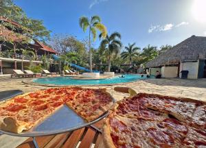 南圣胡安冲浪牧场度假酒店 的两个比萨饼坐在游泳池旁边的桌子上