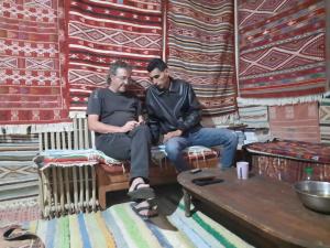 TūjānDar Fatma Toujane的两个人坐在一个地毯的房间的长凳上
