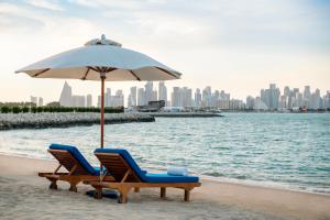 多哈Sharq Village & Spa, a Ritz-Carlton Hotel的海滩上的两把椅子和一把遮阳伞