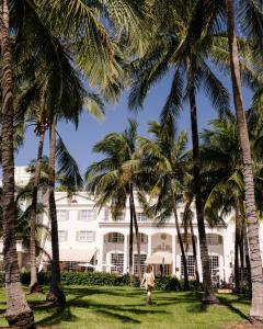迈阿密海滩南海滩贝特西酒店的一位在一座建筑前穿过棕榈树的女人