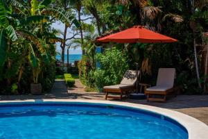 塔马林多The Coast Beachfront Hotel的一个带遮阳伞和两把椅子及一张桌子的游泳池