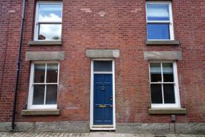 麦克尔斯菲尔德4 Bedroom Town House的一座砖砌建筑,设有蓝色的门和三扇窗户