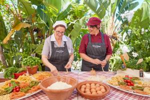 圣玛格利特迪普拉Forte Village Resort - Pineta的两个坐在围裙上的女人站在餐桌旁吃着食物