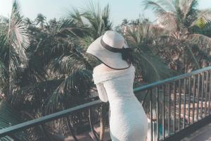会安G Boutique Resort Hoi An的身着白色连衣裙和围栏上戴帽子的女人