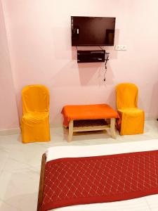 RāmtekHotel Tathastu的一间设有两把橙色椅子和电视的房间