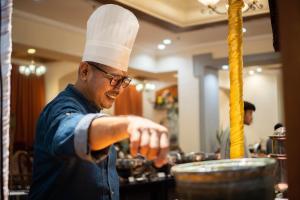 马六甲Grand Swiss-Belhotel Melaka - formerly LaCrista Hotel Melaka的戴着厨师帽准备食物的人