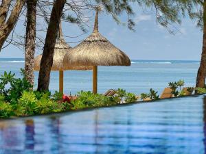 贝隆布尔SO/ Sofitel Mauritius的一个带稻草伞和海洋的游泳池