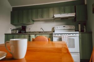 瓦勒多Auberge L'Orpailleur的厨房配有绿色橱柜和带咖啡杯的桌子