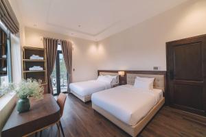 大叻Sunset Hill Dalat的酒店客房设有两张床、一张桌子和一张书桌。