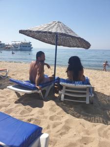 艾瓦勒克Sevo Hotel的两人坐在海滩上,被伞所环绕