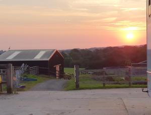 CorscombeKnapp Farm Glamping Puki Pod的红谷仓,背面有日落
