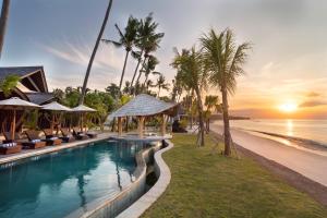 珀尼达岛The Sankara Beach Resort - Nusa Penida的一个带椅子的度假游泳池和日落时的海滩